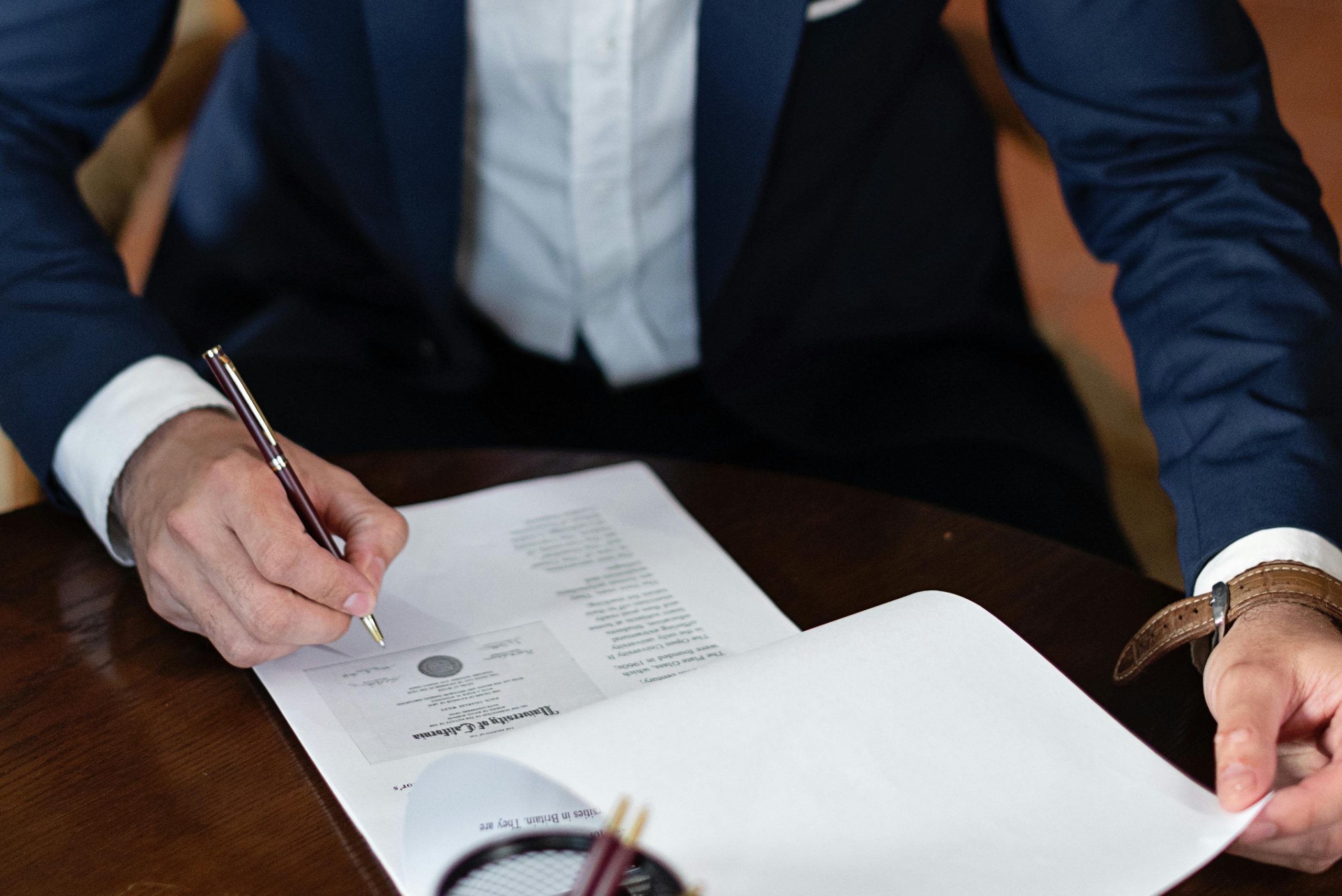 A Man In A Suit Signing Some Documents / Paperwork